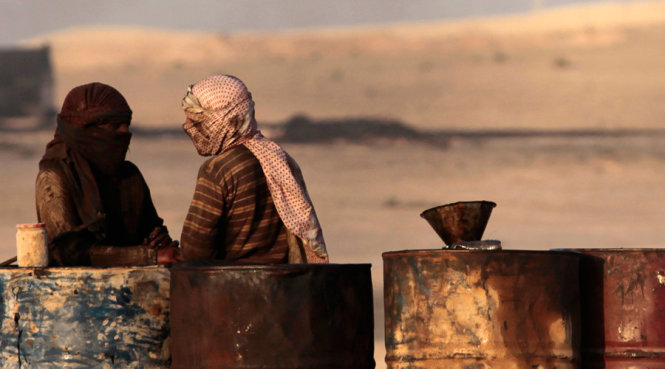 Người dân nói chuyện với nhau khi đứng cạnh các thùng dầu ở cơ sở lọc dầu tại al-Mansoura, Raqqa - Ảnh: Reuters