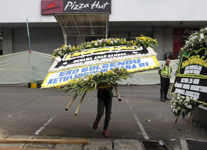 Nhân viên dọn dẹp hoa tưởng niệm các nạn nhân vụ tấn công gần quán cà phê Starbucks ngày 15-1 để cuộc sống trở lại bình thường - Ảnh: Reuters