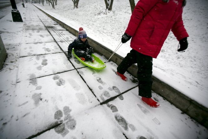 Một phụ nữ kéo theo con nhỏ trên ván trượt trong lúc cơn bão mùa đông đang ập đến Washington - Ảnh: Reuters
