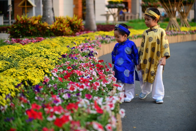 Hai trẻ em mặc áo dài khăn đóng đi dạo vườn hoa.