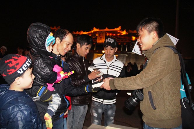 Bạn Tuấn Anh, thành viên chương trình (phải) tặng sách cho người dân, du khách đến quảng trường Ngọ Môn đón giao thừa - Ảnh: PHAN THÀNH