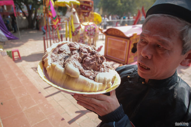 Một bô lão trong làng dâng một miếng thịt đã được luộc chín để làm lễ cúng thánh thần)