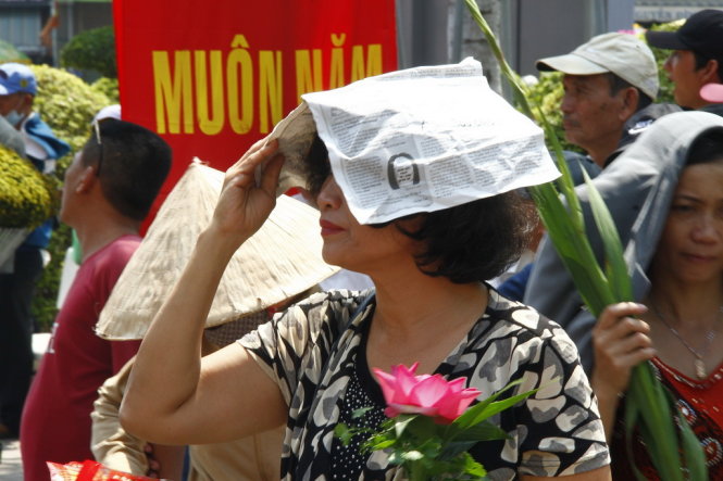 Một phụ nữ dùng tờ báo che nắng để đi lễ - Ảnh: Xuân An