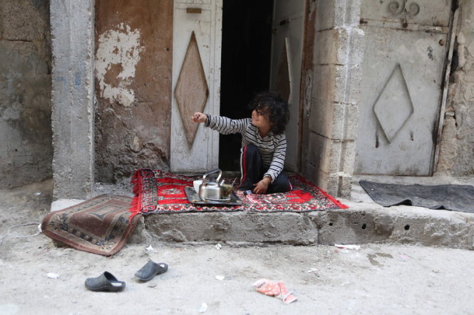 Một em bé ở Tishreen, Syria đang chơi ngoài hiên nhà trong những phút bình yên hiếm hoi của thỏa thuận ngừng bắn - Ảnh: EPA
