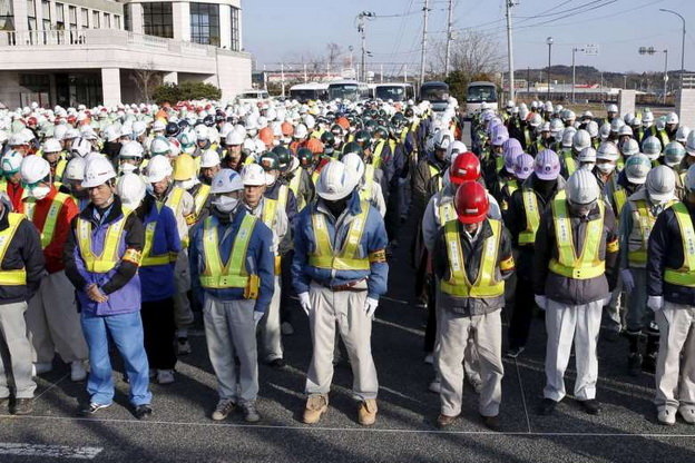 Công nhân khử độc đang mặc niệm nạn nhân động đất-sóng thần ngày 11-3 - Ảnh: Reuters