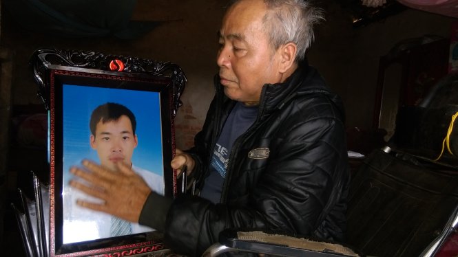Ông Lê Văn Đường, 68 tuổi, ngồi trên xe lăn ôm di ảnh con trai chết bên Angola - Ảnh: Văn Định