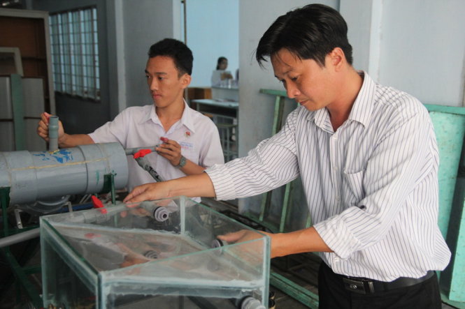 Thầy Trương Hữu Dũng và học trò bên thiết bị chưng cất nước ngọt từ nước mặn bằng năng lượng mặt trời. Hai thầy trò đang cải tiến thiết bị này để chuẩn bị cho ra đời phiên bản sử dụng, có thể sản xuất hàng loạt - Ảnh: Mậu Trường