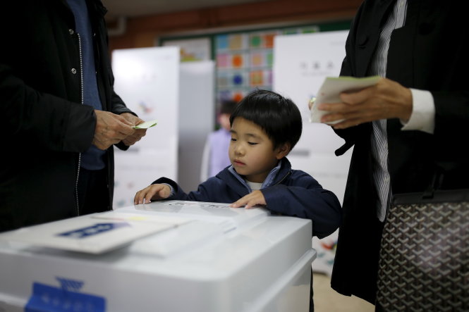 Cậu bé Hàn Quốc theo mẹ đi bầu cử tại Seoul ngày 13-4 - Ảnh: Reuters