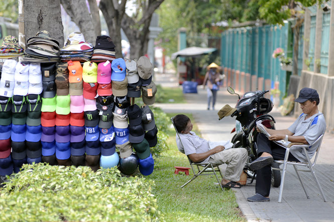 Chú Phạm Hữu Phát (52 tuổi) ngồi dưới gốc cây vừa để tránh nắng vừa bán mũ trên đường Nguyễn Thị Minh Khai (Q.1) - Ảnh: Duyên Phan