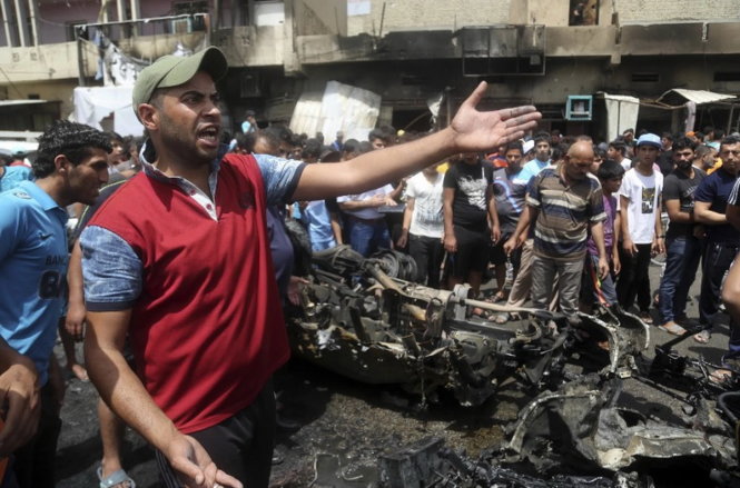 Người dân đứng bên cạnh xác chiếc xe bom nổ trước khu chợ phía đông Sadr City, Iraq ngày 11-5-2016 - Ảnh: AP