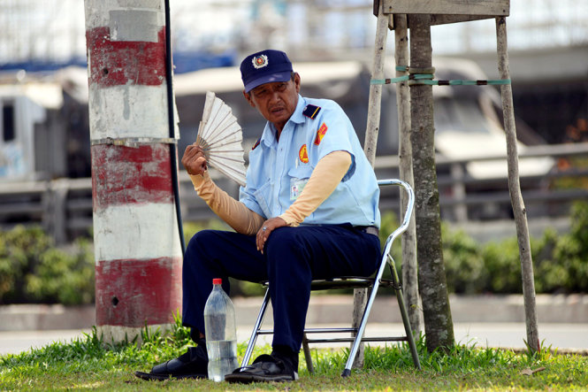 Chú Nguyễn Trung Cang - nhân viên bảo vệ của một công ty trên đường Xa lộ Hà Nội phải dùng găng tay tự chế, vừa ngồi tránh nắng dưới hàng cây xanh đối diện công ty vừa quạt liên tục - Ảnh: Duyên Phan