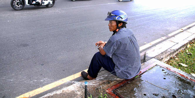 Quá nắng nóng, một người đàn ông ngồi ngay dưới vòi nước tưới cỏ để giải toả cái nóng - Ảnh: Ngọc Dương