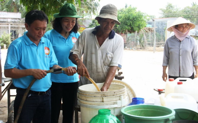 Ông Trần Văn Ghê (áo trắng, 63 tuổi) đang lấy nước tại một giếng nước tập thể tại xã An Hiệp - Ảnh: Lê Phan