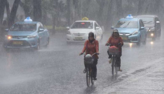 Hai người phụ nữ đạp xe trong cơn mưa lớn tại tỉnh Trung Java - Ảnh: JAKARTA POST