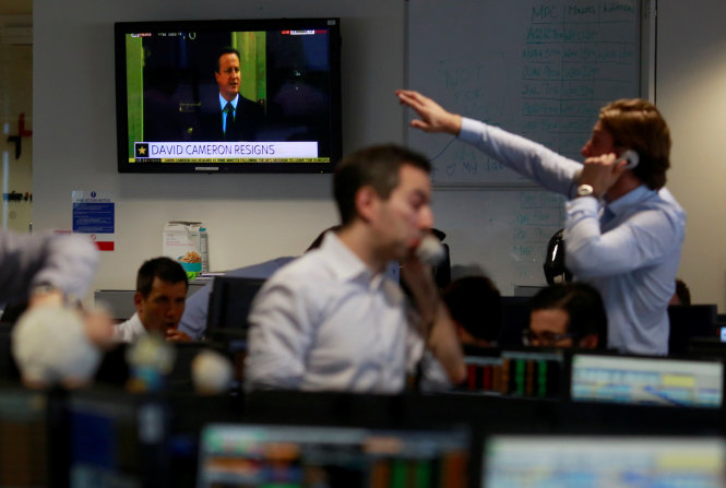 Nhân viên văn phòng tại một trụ sở ở London theo dõi thông tin thủ tướng David Cameron từ chức - Ảnh: REUTERS