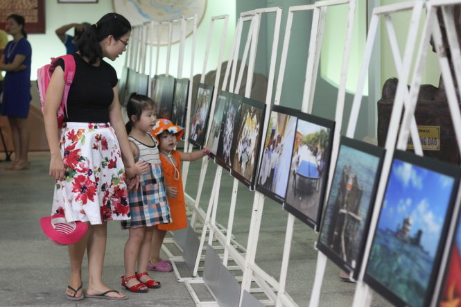 Chị Hoàng Xuân Cúc (30 tuổi, ở Quán Nam, TP Hải Phòng) chỉ cho hai cô con gái nhỏ những bức ảnh chụp về Trường Sa tại triển lãm - Ảnh: Tiến Thắng
