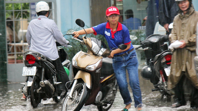 Các tình nguyện viên bì bõm dẫn xe cho phụ huynh dưới cơn mưa sau buổi thi - Ảnh: MẬU TRƯỜNG