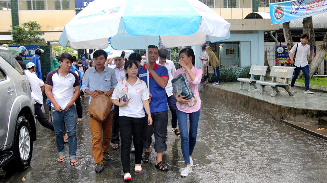 Các tình nguyện viên dùng dù lớn để đưa thí sinh rời khỏi điểm thi sau buổi thi  - Ảnh: MẬU TRƯỜNG