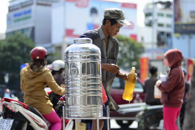 Một người lao động ghé vào bình nước tại ngã bảy Lý Thái Tổ để uống trà đá miễn phí - Ảnh: Duyên Phan