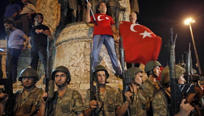 Người dân ủng hộ tổng thống Erdogan vẫy cờ Thổ Nhĩ Kỳ tại quảng trường Taksim. Trước đó, quân đảo chính tuyên bố chiếm được quảng trường. Trong ảnh các binh lính vẫn tỏ ra khá bình tĩnh, đứng chung với người dân ủng hộ ông Erdogan - Ảnh: REUTERS