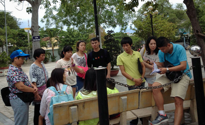 Hướng dẫn viên người Trung Quốc (bìa phải) ngồi viết danh sách đoàn du lịch trong khuôn viên nhà thờ Núi (TP Nha Trang) chiều 19-7 - Ảnh: TIẾN THÀNH