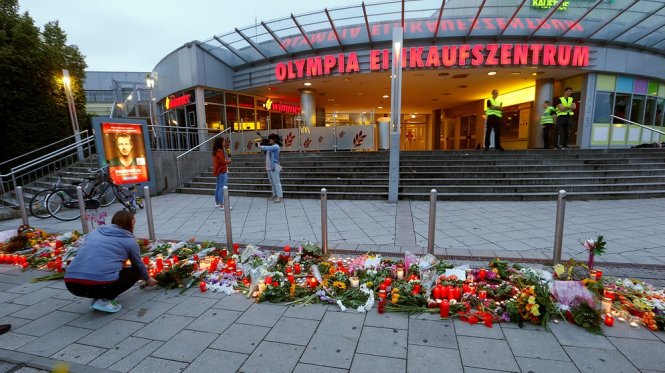 Một vụ nổ chưa rõ nguyên nhân làm 1 người chết và 10 người bị thương, cơ quan nội vụ bang Bavaria cho rằng đây không phải một tai nạn thông thường. Trong ảnh, người dân đặt hoa tưởng niệm các nạn nhân vụ xả súng ở trung tâm thương mại Olympia - Ảnh: Br.de