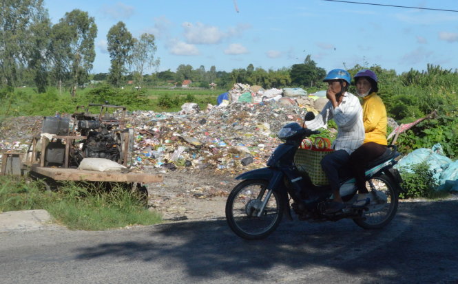 Người đi xe máy phải một tay chạy xe một tay bị mũi vì mùi hôi thối từ bãi rác Tân Phú, huyện Thanh Bình - Ảnh: NGỌC TÀI
