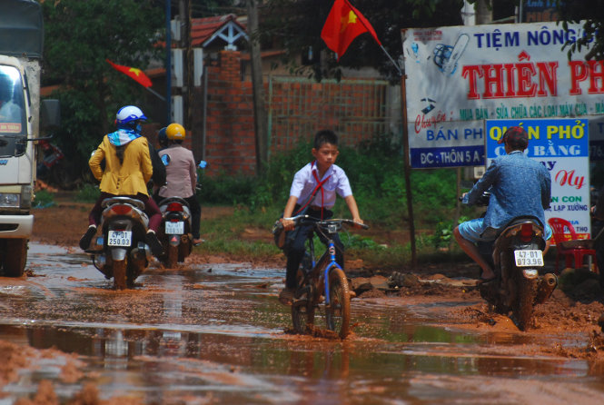 Một học sinh đạp xe bì bõm giữa tuyến đường ngập ngụa bùn đục dẫn qua trung tâm xã Ea Wy để tới trường