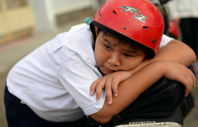 Một học sinh mệt mỏi nằm gục trên yên xe sau khi đi bộ qua đoạn ngập nước - Ảnh: HỮU KHOA