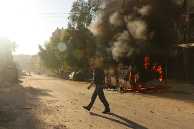 Một người đàn ông Syria đi qua khu vực có chiếc xe bus đang bốc cháy sau một đợt không kích tại quận Salaheddin do lực lượng nổi dậy kiểm soát ở Aleppo ngày 25-9 - Ảnh: AFP