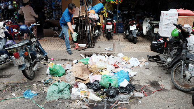 Người đàn ông vứt rác vào đống rác lớn bên cạnh miệng cống thoát nước trên đường Trần Bình sát chợ Bình Tây, TP.HCM - Ảnh: HỮU THUẬN
