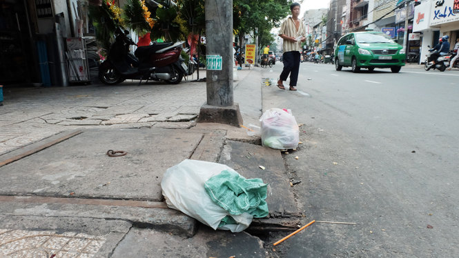 Cống thoát nước trên đường Võ Văn Tần, P.5, Q.3, TP.HCM bị chặn kín miệng bởi rác và miếng gỗ để cho xe máy lên xuống - Ảnh: HỮU THUẬN