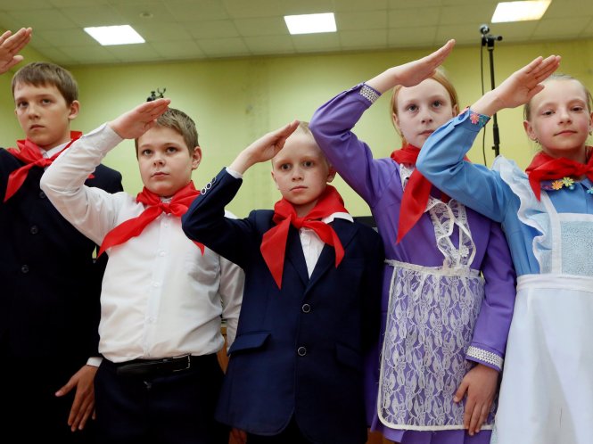 Các em học sinh đeo khăn quàng đỏ đang giơ tay chào trong một buổi lễ tại trường ở thành phố  Krasnoyarsk vùng Siberia, Nga - Ảnh: Reuters