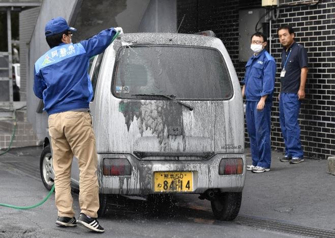 Người dân ở Aso rửa tro núi lửa bám trên xe - Ảnh: REUTERS