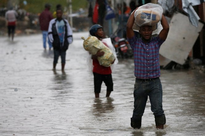 Người dân mang vác tư trang đồ đạc lội qua những con phố ngập nước - Ảnh: Reuters