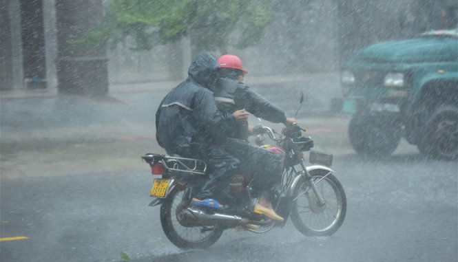 Hai người cố gắng chạy xe máy khi trời mưa, gió rất lớn tại đảo Hải Nam - Ảnh: Tân Hoa Xã