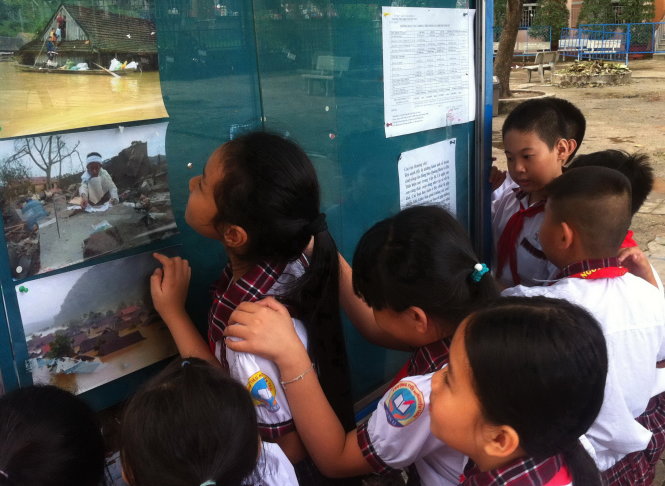 Học sinh Trường tiểu học Nguyễn Trãi xem những tấm ảnh về lũ lụt ở miền Trung được dán ở bảng thông báo - Ảnh: HÀ BÌNH