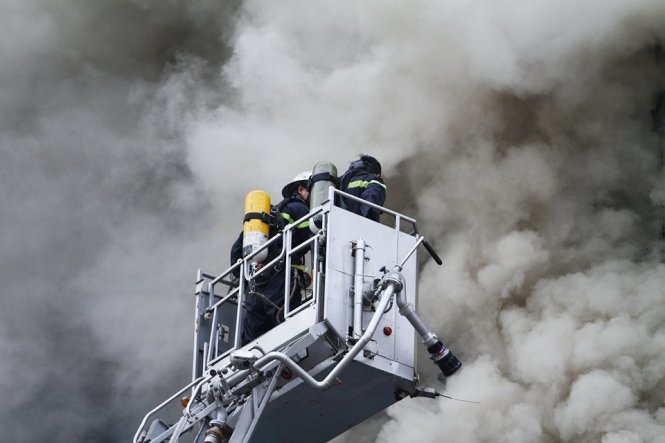 Xe nâng đưa lính cứu hỏa lên cao để phun nước dập lửa - Ảnh: N.Trần