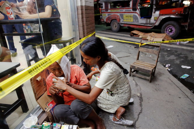 Người dân trợ giúp một người bán hàng rong thất thần khi thấy thi thể người bị bắn ở Manila hôm 18-10. Trên xe đậu gần thi thể có tấm biển ghi dòng chữ 