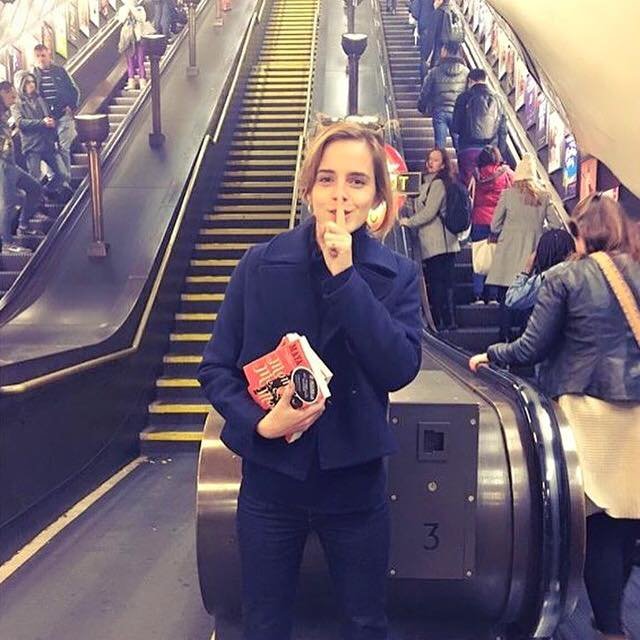 Emma Watson đứng bên cầu thang băng chuyền tại một ga tàu điện ngầm ở London với những cuốn sách cô sẽ giấu tặng ở đâu đó cho bạn đọc - Ảnh: Facebook/Books on the Underground