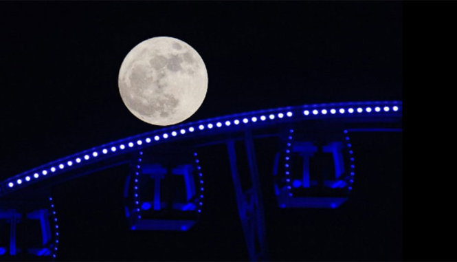 Siêu trăng đi qua một vòng đu quay - Ảnh: AFP