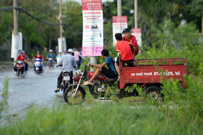 Một chiếc ba gác hờ chở xe máy thuê qua đoạn ngập nước trên đường Lê Văn Lương - Ảnh: HỮU KHOA