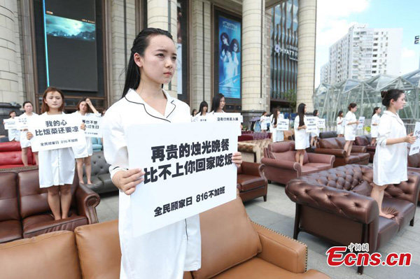 Những người phụ nữ đứng trên ghế sofa với các tờ giấy có nội dung lên án những ảnh hưởng của chuyện làm việc quá tải đối với đời sống gia đình họ trong một sự kiện tại Thượng Hải ngày 8-8-2016. Một trong những người cầm tấm biển ghi 
