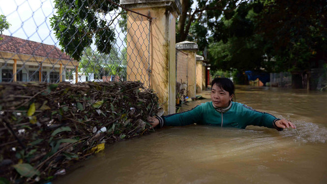 Chị Nguyễn Thị Thanh Mai (huyện Tuy Phước) phải bám vào hàng rào để di chuyển về nhà trong dòng nước ngập sâu và chảy mạnh - Ảnh: HỮU KHOA