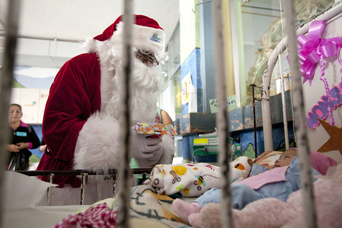 “Ông già Noel” viếng thăm và tặng quà cho một đứa trẻ tại bệnh viện San Juan de Dios ở Guatemala - Ảnh: AP