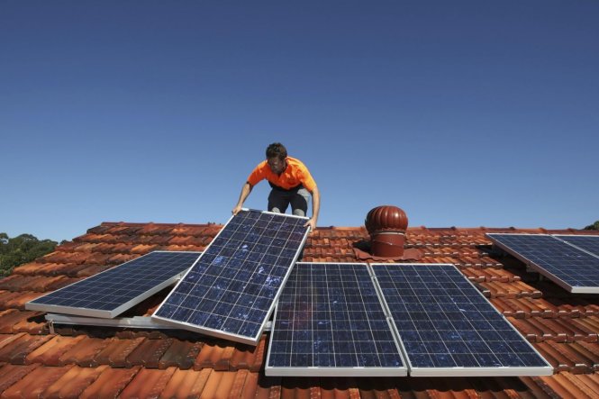 Một người thợ lắp đặt các tấm thu năng lượng mặt trời trên mái một căn nhà ở Sydney, Úc - Ảnh: Reuters