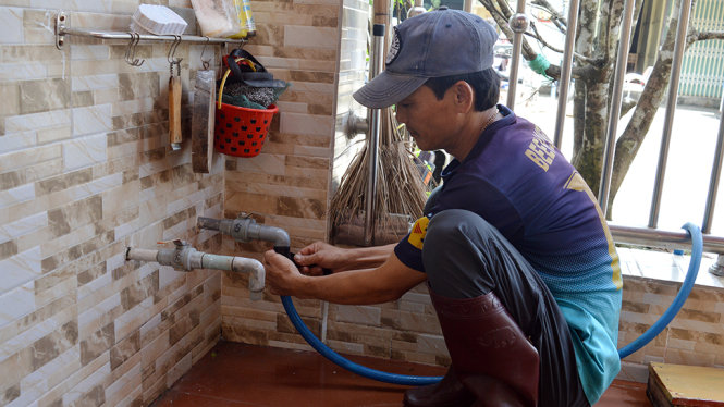 Anh Trần Thanh Vân (45 tuổi, ngụ khu phố 4) đang lắp đặt ống dẫn nước từ giếng nhà mình cho hàng xóm xài tạm - Ảnh: H.Trung