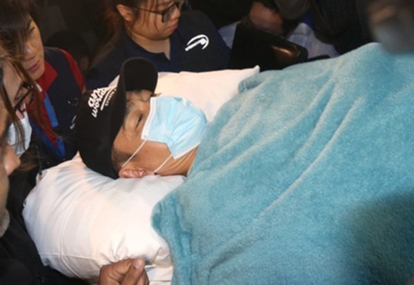 Lưu Đức Hoa được đưa từ sân bay Hong Kong đến bệnh viện Dưỡng Hòa, tuy nằm bất động trên băng ca nhưng tinh thần của anh khá tốt, trên trán thấy rõ vết trầy xước do xây xát - Ảnh: Oriental Daily