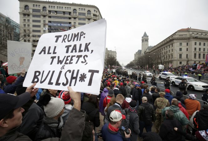 Một người biểu tình cầm tấm biển đứng trong đoàn người chờ tổng thống Donald Trump diễu hành qua tại Washington - Ảnh: Reuters