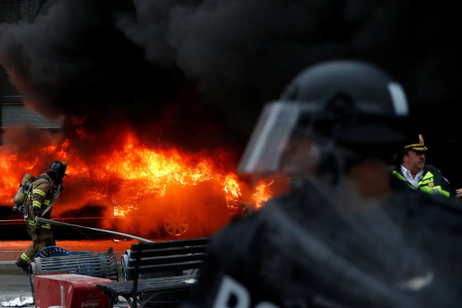 Cảnh sát và lính cứu hỏa đứng gần một chiếc xe do người biểu tình đốt để phản đối ông Trump trong ngày nhậm chức tại Washington DC - Ảnh: Reuters